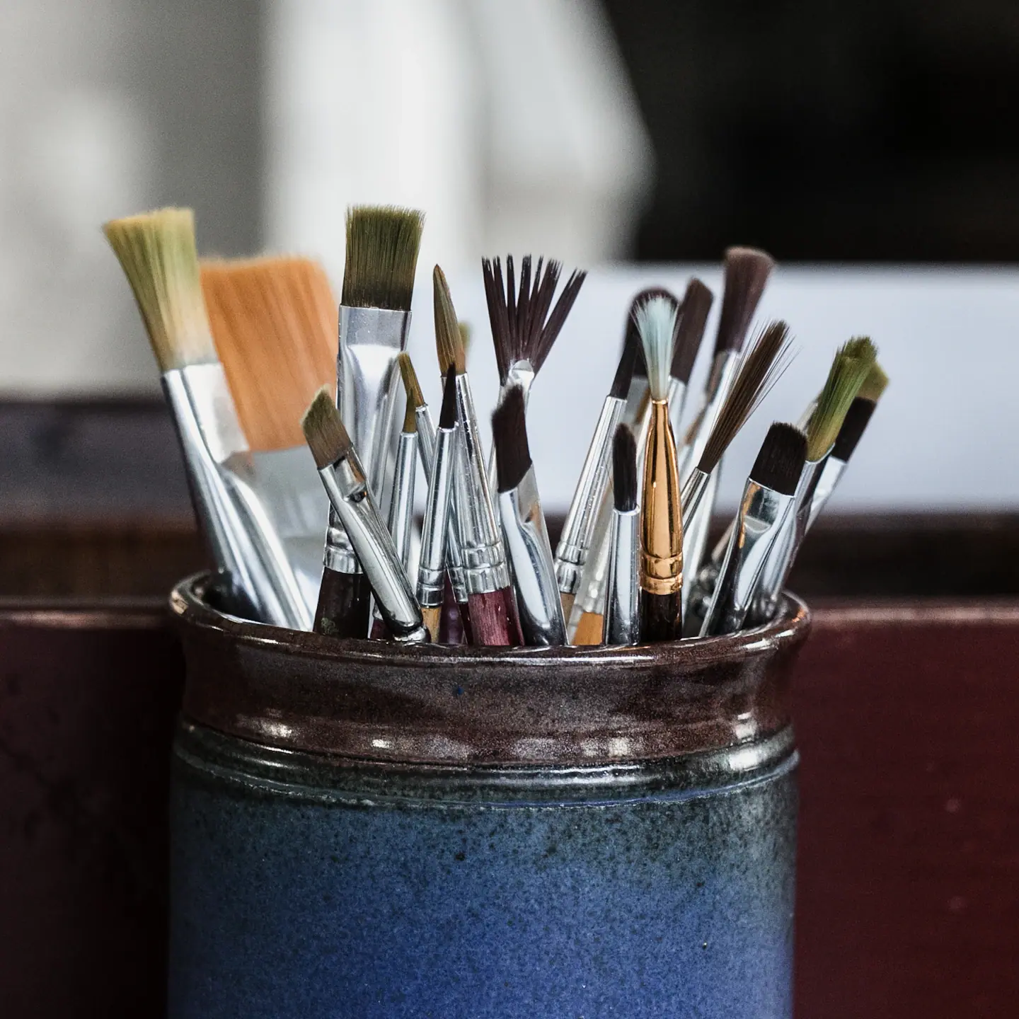 Assorted paintbrushes standing in a blue ceramic pot.